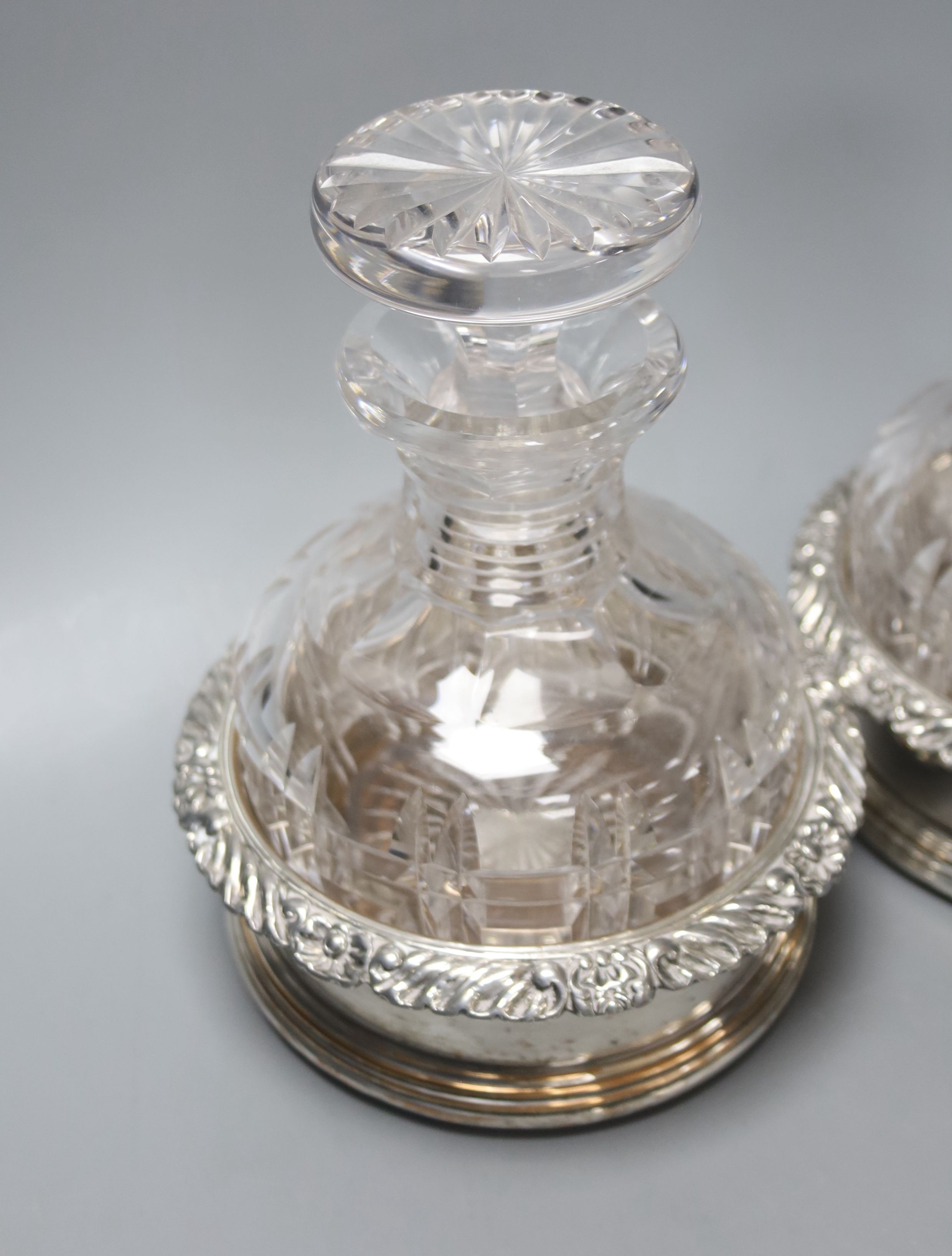 A pair of silver plated coasters with cut glass decanters. 20cm